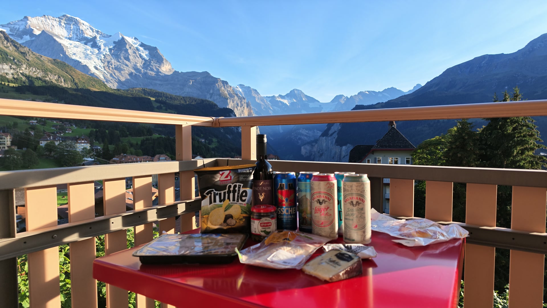 山々を背景に赤いテーブルへ並べたビールとおつまみ